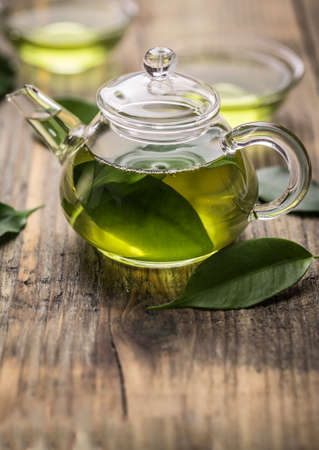 Glass teapot with green tea leaves on wooden surfaceの写真素材