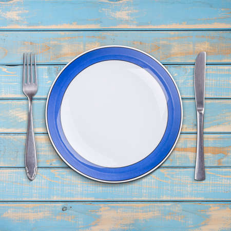Fork with knife and blank plate, on blue wooden table backgroundの写真素材