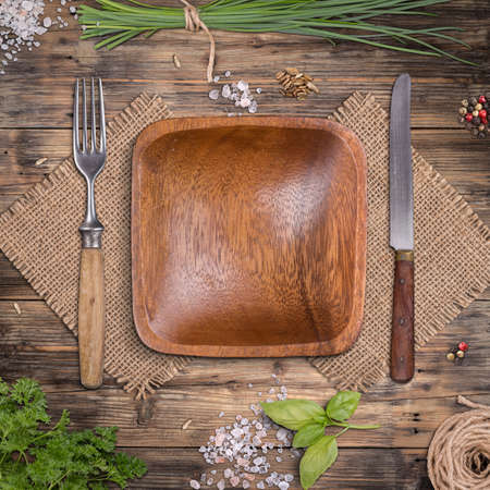 Empty wooden plate on weathered wooden table with herbsの写真素材