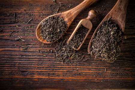Spoon of dried green tea leaves on wooden backgroundの写真素材