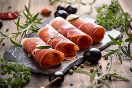Sliced prosciutto with herbs and oliveの写真素材