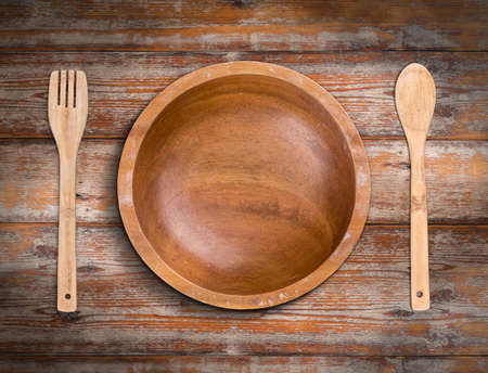 Wooden bowl with fork and spoon on weathered wooden backgroundの写真素材