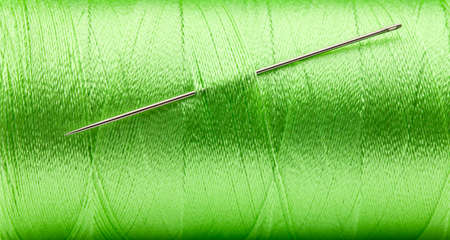 Sewing needle in green thread bobbin close up