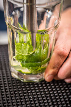 Bartender crushes mint and lime for preparation mojito cocktailの写真素材