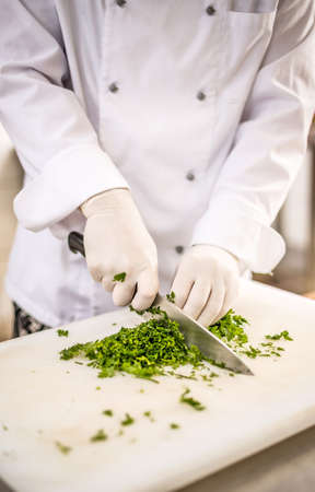 Chef chopping parsley leaves with a knife on a cutting boardの写真素材
