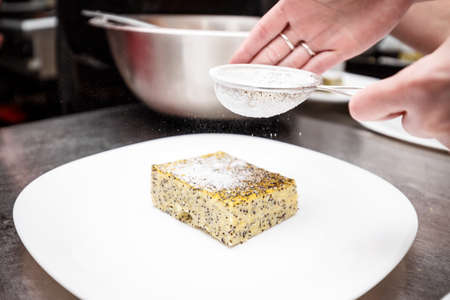 Chef hand sprinkling icing sugar over fresh polenta cakeの写真素材