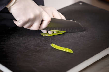 Chef cutting fresh green peas on black cutting boardの写真素材