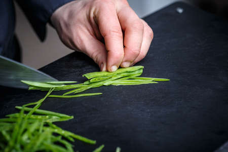 Chef cutting chives on the black cutting board