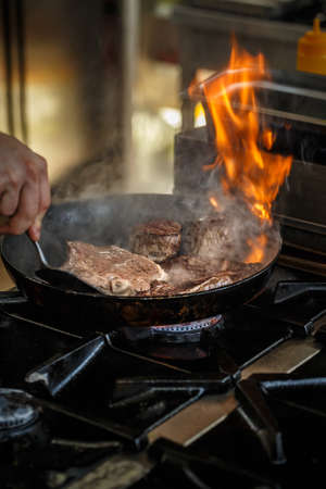 Chef frying meat steak on the gas stove with fire at the kitchenの写真素材