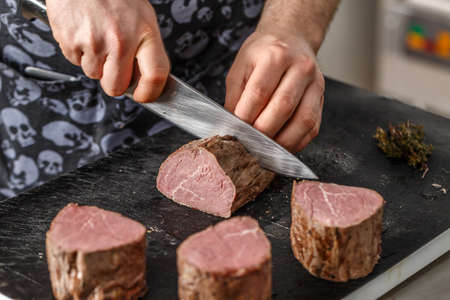 Chef is cutting boiled beef meat on black chopping boardの写真素材