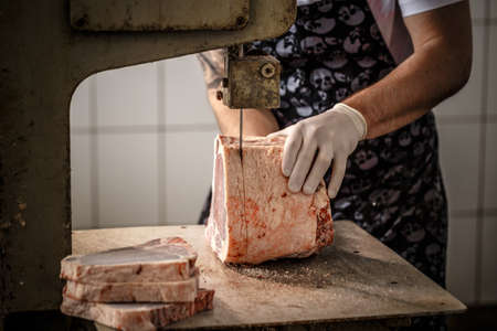 Worker cuts onto equal pieces frozen beef meat in work shop at the factory.の写真素材