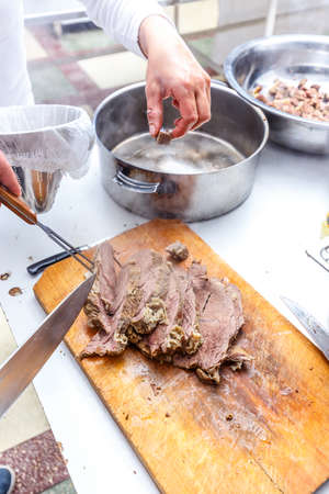 The cook cuts boiled beef meat on wooden cutting boardの写真素材