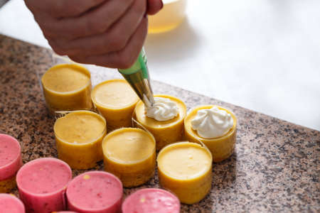 Woman hand decorating mini cakes with pastry cream