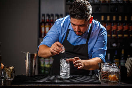 Barman puts the ice cubes into a glass, bartender is working