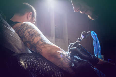 Portrait of a man tattoo master showing a process of tattoo creation in a man's hand under the lamplightの写真素材