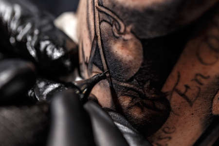 A professional tattoo artist introduces black ink into the skin using a needle from a tattoo machine.の写真素材