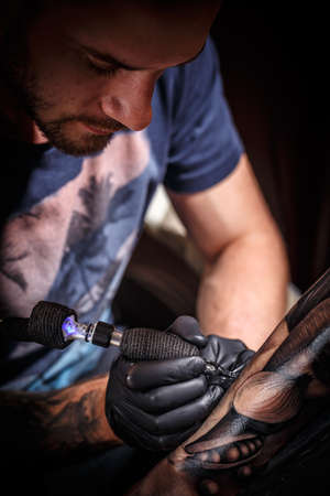 Close up tattoo artist demonstrates the process of getting black tattoo の写真素材
