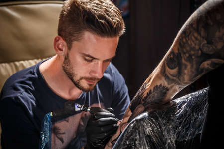 Professional tattoo artist makes a tattoo on a young man's hand