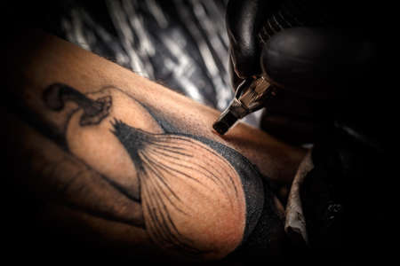 Close up tattoo artist demonstrates the process of getting black tattoo with paintの写真素材