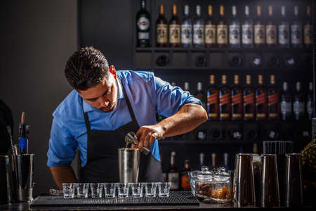 Bartender with jigger pouring alcohol into shaker and preparing cocktail at bar counterの写真素材