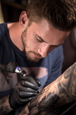 Professional tattoo artist makes a tattoo on a young man's handの写真素材