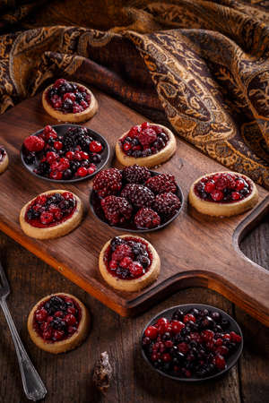 Delicious berry fruits mini tarts (tartlets) on wooden backgroundの写真素材