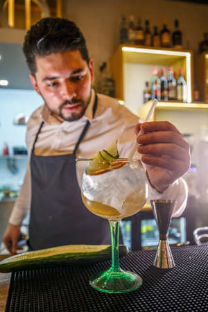 Expert barman is decorating cocktail with cucumberの写真素材