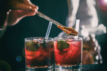 Bartender is adding lemon to the red cocktail at bar counterの写真素材