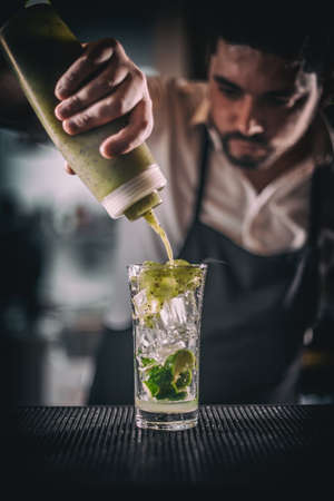 Barman pouring sweet syrup into the fresh sour lime and kiwi cocktail on the bar counterの写真素材