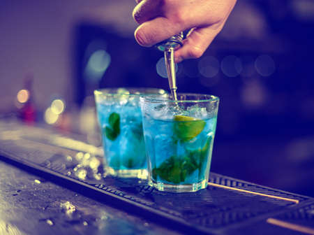Bartender is pouring blue syrup into the glass with ice cubes on the bar counterの写真素材