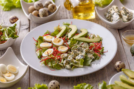 Plate of salad with avocadoes, quail egg, blue cheese and greens on wooden table