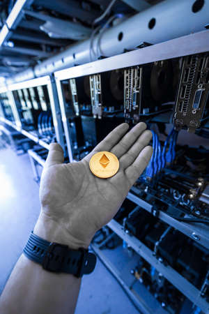 Hand holding golden etherium coin, cryptocurrency mining unitの写真素材