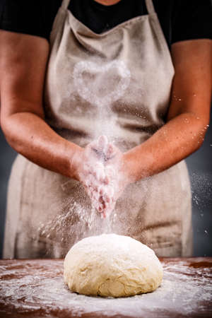 Woman sprinkling flour over fresh dough on kitchen table