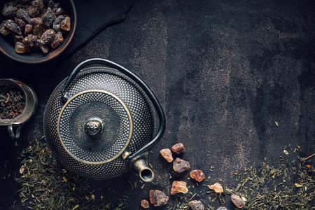 Teapot, rock of sugar and assortment of dry tea on black table. Top view with copy spaceの写真素材