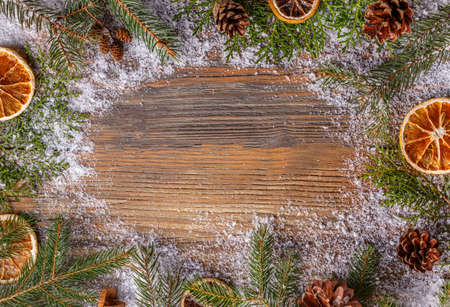 Christmas frame made of fir branches, pine cones and dried orange slices on snowy wooden table
