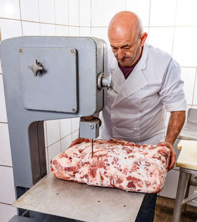 Male butcher cutting meat on bandsaw at meat factoryの写真素材