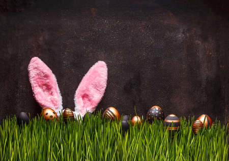 Cute Easter scene with pink rabbit ears and eggs hiding in green grass 