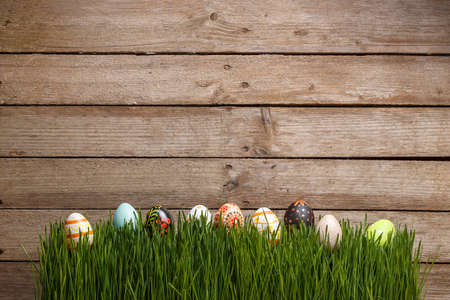 Decorated Easter eggs in the grass on wooden background, copy space