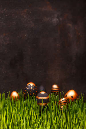 Easter composition with golden and black eggs hiding in green grass, copy space