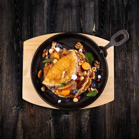 Delicious sweet pancakes served on a cooking pan with fresh fruits, nuts and chocolate sauceの写真素材