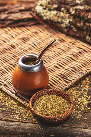 Composition of yerba mate South American tea, dried leaves in wooden bowl and mate calabash with...