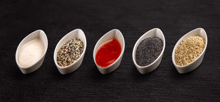 White ceramic bowl with different sauce and seeds on black backgroundの写真素材