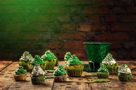 Happy St Patricks Day cupcakes with green theme decorations on vintage style wood background.