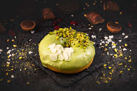 Donut in green glaze with pistachio and almond flakes on black slate backgroundの写真素材