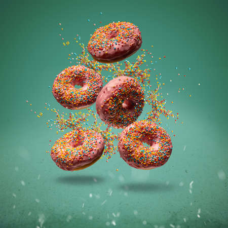 Flying sweet donuts with sprinkels on green backgroundの写真素材