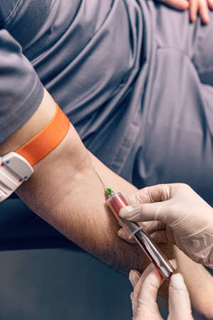 Nurse injecting male patient with syringe to collect blood sampleの写真素材