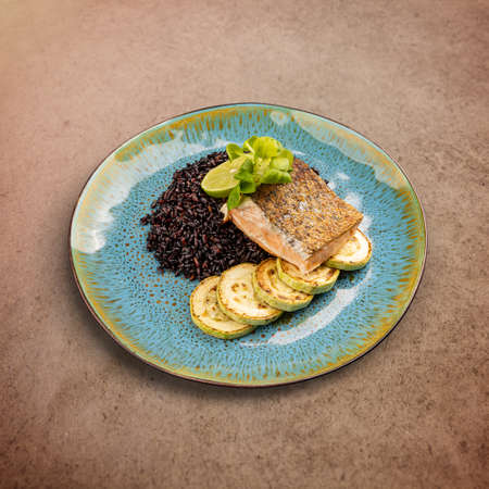 Fried salmon steak with black rice and grilled zucchiniの写真素材
