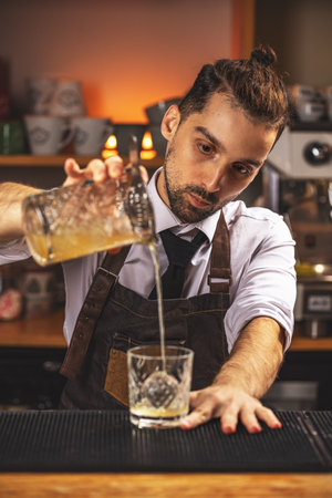 Bartender making cocktail in glass on bar counterの写真素材