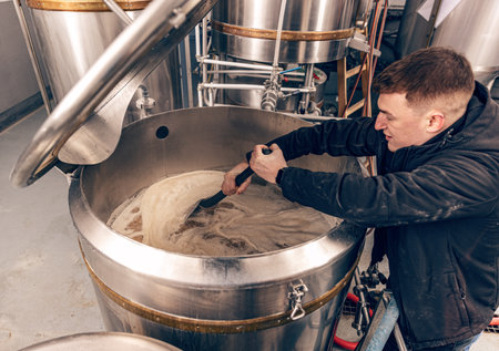 Brewery worker controlling process of craft beer production, stirring raw materials in fermenterの写真素材