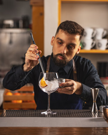 Professional bartender prepare a fresh cocktail in the glass with an ice at the steel barstand